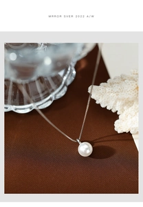 Detail view of a white round pearl pendant on a delicate silver chain with coral props