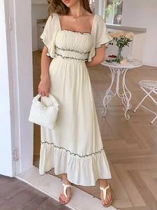 Détail de la robe longue crème à encolure carrée avec volants noirs et sac à main blanc
