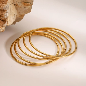 Macro shot of minimalist gold stainless steel bangles stacked with a natural stone accent