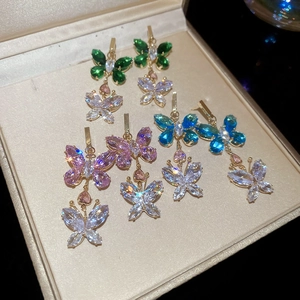 Detailed macro view of gold butterfly earrings with colorful inlaid crystals in a beige box