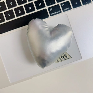 Detail of a metallic silver heart plush charm with woven label on a laptop surface