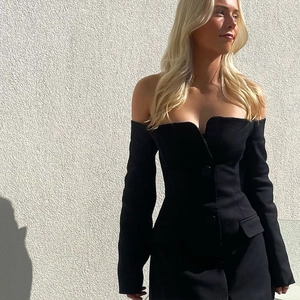 Detail of a black off-shoulder dress with long sleeves, button decor and flap pockets