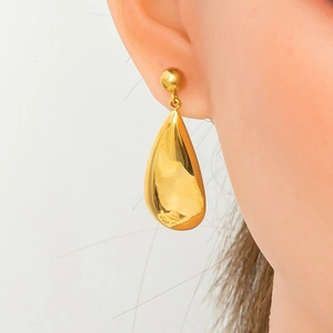 Detailed view of polished gold teardrop pendant earrings worn on model for scale