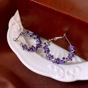 Silver needle hoop earrings with large purple crystals on a luxury display