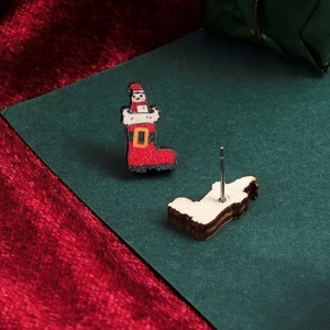 Detail of hand-painted wooden Santa Claus and boot earrings with festive velvet background