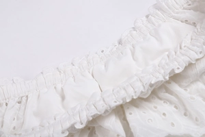 Détail de la broderie florale ajourée blanche et du tissu plissé élastique à la taille