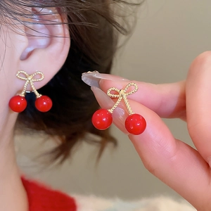 Close-up of elegant cherry bow earrings worn on ear showing resin beads and golden texture