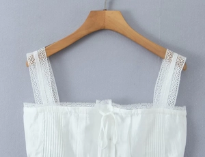 Close-up of white camisole top featuring intricate lace trim and pleated fabric details