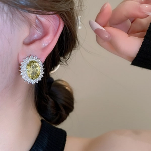 Detail view of silver stud earrings with oval yellow gemstone and zircon halo on model