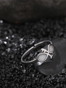 Macro shot of silver adjustable metal ring with white stones on black volcanic rocks