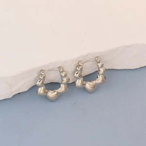 Detailed close-up of heart-shaped silver earrings on a white textured stone surface