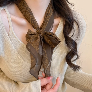 Detail of a brown paisley print silk scarf necklace paired with a beige knit sweater