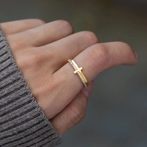 Close-up of a gold cross ring with pavé zircons worn on index finger over grey knitwear