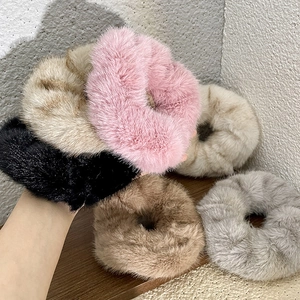 Hand holding assorted plush velvet scrunchies in pink, beige, and grey soft colors