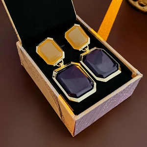 Detail of geometric earrings with yellow and purple stones in a textured gift box