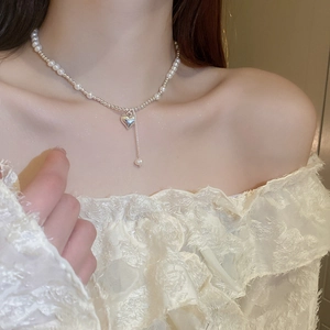 Detail of sweet heart pendant and pearl choker necklace worn on a woman's collarbone