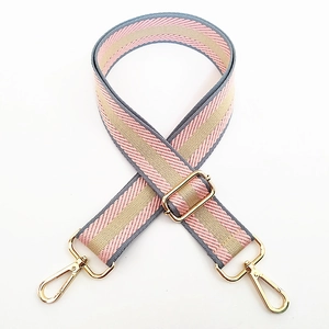 Detail of adjustable woven handbag strap in pink and grey stripes with gold metal hooks