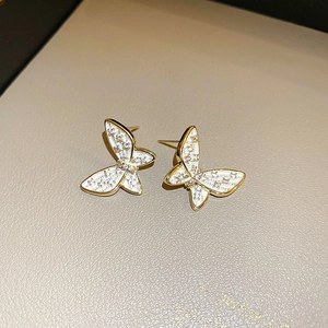 Elegant gold butterfly earrings with white enamel and sparkling zircon stones on beige leather