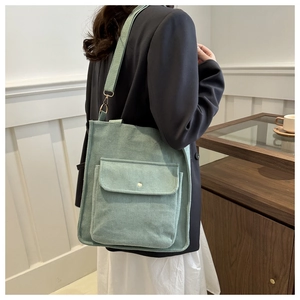Detail view of mint green corduroy shoulder bag featuring a front pocket with metal snap button