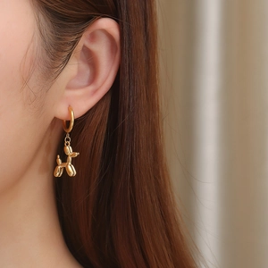 Close-up of a high-polished golden balloon dog earring worn by a model in warm light