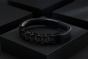 Detail shot of men's black leather braided bracelet with metal chain links on a dark pedestal