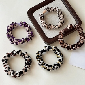 Close-up of five assorted leopard print velvet scrunchies on a wooden display tray