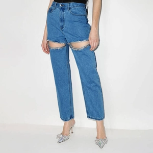 Détail d'un jean bleu taille haute avec des découpes en strass sur la cuisse