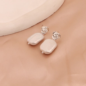 Detailed macro view of silver rose stud earrings with rectangular white baroque pearls