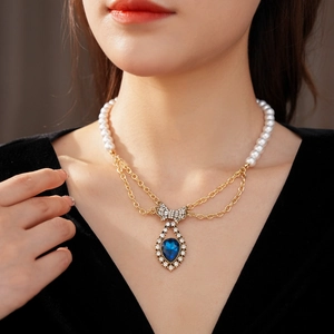 Close-up of vintage gold pearl necklace with diamond bow and blue teardrop pendant