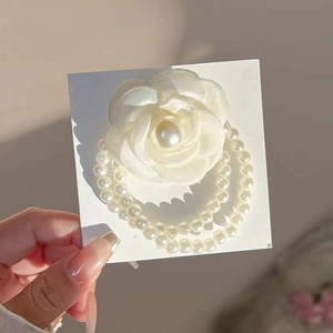Detail of white camellia flower hair tie with double-row white pearl chains on white card