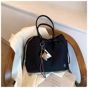 Detail of black drawstring tote bag with baseball pendant and metal flower logo charm
