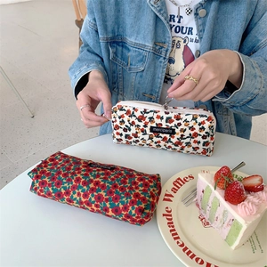 Close-up of floral corduroy pencil case in beige and red floral patterns on a cafe table