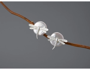 Macro detail of S925 silver dragonfly stud earrings with white pearls on a natural wood branch