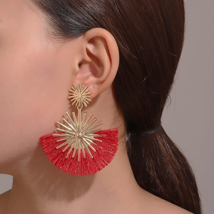 Detail shot of red fan-shaped fringe earrings with golden sunburst metal on model