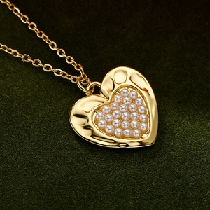 Elegant gold heart pendant necklace with white pearls and hammered texture on green velvet