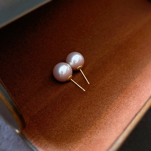 Close-up of pink pearl earrings with gold needles on a textured brown jewelry box