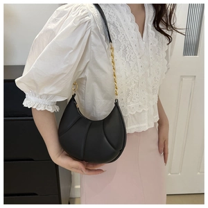 Detail of black crescent shoulder bag with quilted texture and gold chain strap