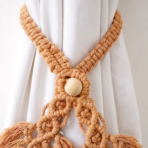 Detail of bohemian hand-woven beige cotton curtain tieback with wooden bead and tassels