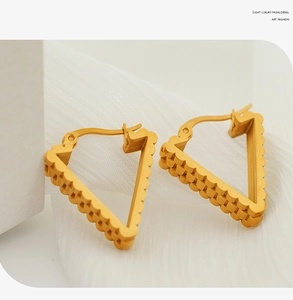 Macro shot of gold triangular earrings with textured wavy edges on white silk texture