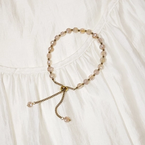 Detail of adjustable golden bracelet featuring pink faceted crystals on soft white fabric