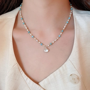 Dettaglio di una collana di perline con pendente ovale su un abito di lino beige