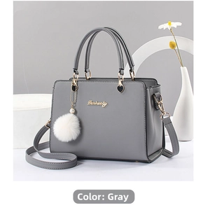 Detail of grey crossbody bag featuring golden hardware and a white faux fur pompom charm