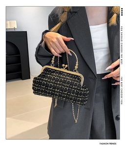 Detail of vintage black handbag with gold lattice pattern and metal chain worn by model