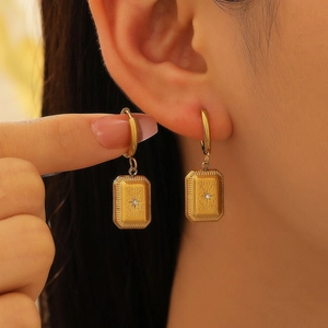 Gros plan de boucles d'oreilles rectangulaires dorées avec texture soleil et zircon