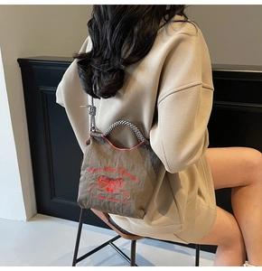 Detail of brown nylon bag featuring red cherry embroidery and bow-knot accent with checkered straps
