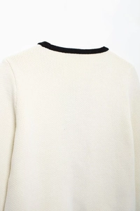 Gros plan du cardigan en maille crème avec bordure noire élégante au niveau du décolleté