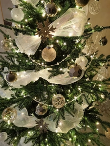 Close-up of champagne gold ornaments and white mesh ribbon on a lush Christmas tree