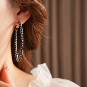 Close-up of model wearing large round black leather hoop earrings with white NICE patterns