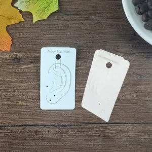 Detail of 4x7cm white jewelry display card with ear silhouette on wood background