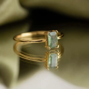 Detail of a rectangular green stone ring with four-prong gold plated setting and mirror reflection